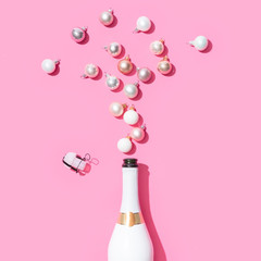 White champagne bottle with Christmas baubles decoration on pink background. Flat lay. Minimal party concept.