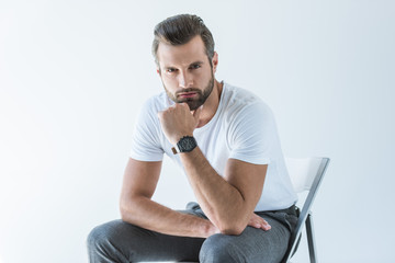 fashionable handsome man in white t-shirt with wristwatch sitting on chair, isolated on white