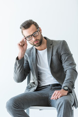 handsome confident businessman in gray suit sitting on chair, isolated on white