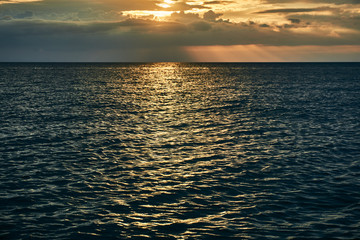 Beautiful bright orange sunset beyond the horizon line of the sea and reflection of the last rays on the surface of the water