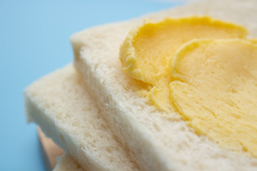 White no crust sandwich bread slices with sweet margarine on chopping board, on blue background
