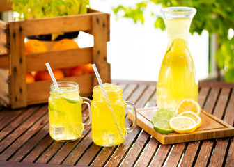Mason jar glasses of homemade lemonade with slices of lemon on wooden table outside