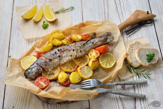 Gebackene Zitronen-Forelle mit leckerem Ofengem&uuml;se serviert auf Backpapier &ndash; Baked lemon trout with oven-roasted rosemary potatoes and tomatoes, served on baking paper