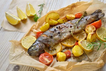 Foto op Canvas Gebackene Zitronen-Forelle mit leckerem Ofengemüse serviert auf Backpapier – Baked lemon trout with oven-roasted rosemary potatoes and tomatoes, served on baking paper © kab-vision