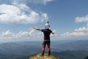Father holding little girl on his shoulder while on top of the mountain. Sunny summer day. Freedom and parenting