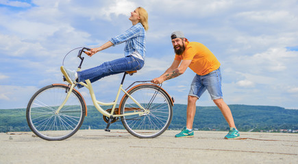 Learn cycling with support. Cycling technique. Woman rides bicycle sky background. Man helps keep balance and ride bike. How to learn to ride bike as adult. Girl cycling while boyfriend support her