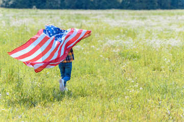back view of child running in field with american flag in hands