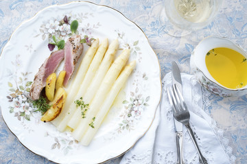 Traditional sliced pork fillet steak with white asparagus in butter sauce and roast potatoes as top view on a classical plate