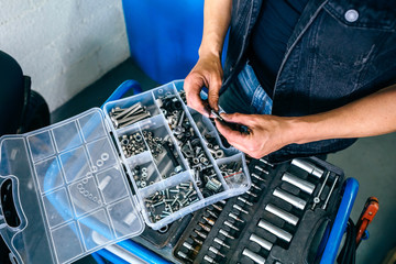 Detail of mechanic's hands choosing screws and nuts from a tool box in the workshop