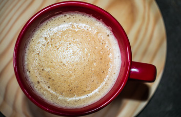  red cup with coffee with milk in a round wooden tray