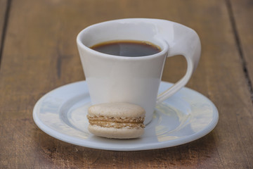 Beautiful white cup of espresso and one macaroon on wooden background close up