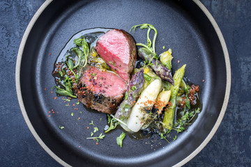 Modern German asparagus potato salad with barbecue dry aged sliced fillet steak and herbs as closeup on a plate