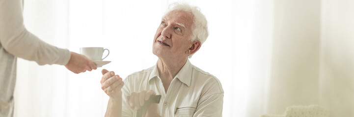 Panorama of happy elderly man with walking stick taking tea