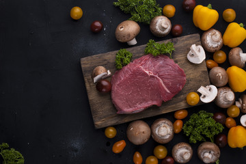 Steak meat on a black background. Beef and vegetables and mushrooms for cooking dinner. Free space for text. Top view