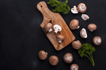 Mushrooms champignons on a black background and a wooden board. Ingredients for lunch. Free space for text. Top view