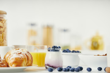 close up view of healthy yogurt with fresh blueberries and croissant for breakfast on white tabletop