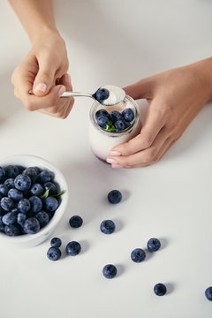 Cropped Shot Of Woman With Yogurt And Fresh Blueberries For Breakfast On White Tabletop