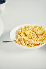 close up view of spoon and corn flakes with milk in bowl for breakfast on white surface