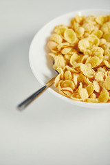 close up view of spoon and corn flakes with milk in bowl for breakfast on white surface