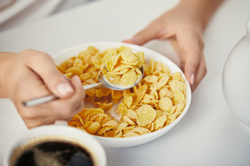 partial view of woman at table with corn flakes and cup of coffee for breakfast