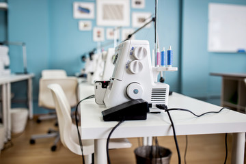 A white electric sewing machine is standing on the white table in the tailor's room.