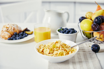 close up view of tasty breakfast with corn flakes and glass of juice on white surface
