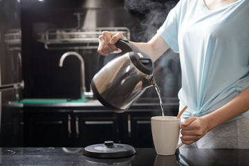 Anonymous female filling mug with hot water while brewing beverage in kitchen