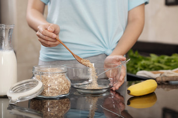 Crop lady using spoon to put oatmeal in bowl while preparing breakfast in kitchen