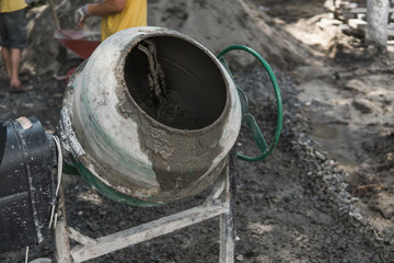 Construction worker add ingredients for mixing in the concrete mixer at building site using shovel...