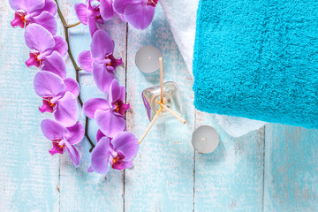 Towel, a branch of an orchid, candles and aroma sticks on a wooden, blue background. Spa treatments, hygiene, bathroom, shower. Spa. Top view