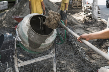 Construction worker add ingredients for mixing in the concrete mixer at building site using shovel...