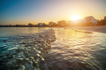 Obraz premium Wavy curves of sea is covered in golden sunset light. Sea at sunset sunlight. Wavy curves pattern on beach. Waves in bokeh focud