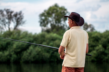 A fisherman in shorts and hat is fishing on the shore of the lake. Fishing, recreation