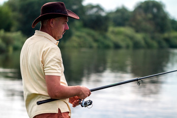 A fisherman in shorts and hat is fishing on the shore of the lake. Fishing