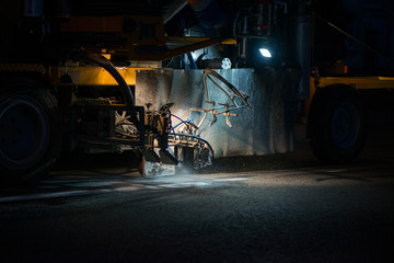 Thermoplastic spray marking machine during road construction works at night. Traffic line painting on asphalt