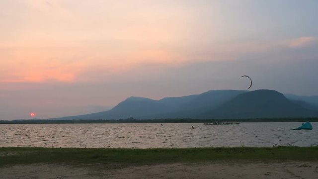 Kitesurfer swimming close to the sea coast. Beautiful orange sunset and Bokor mountain at the distance. Kampot, Cambodia. 