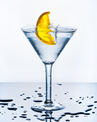 Orange slice splashing in drinking glass. Backlit studio image.