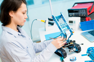 Student girl in electronics laboratory, experiment with microcontroller and robot cnc module