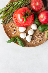 Mozzarella and tomato with basil leaves, rosemary and thyme on a wooden plate. Ingredients for Italian salad caprese.  Copy space