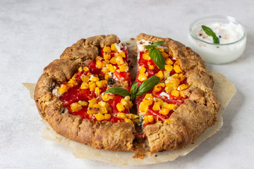 Homemade rustic open pie (galette) with tomato and sweet corn with fresh basil and greek yogurt on white background.