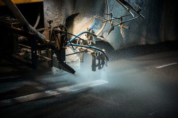 Thermoplastic spray marking machine during road construction works at night. Traffic line painting on asphalt