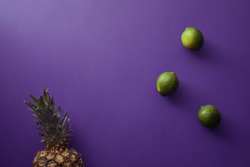 top view of pineapple and limes on violet surface