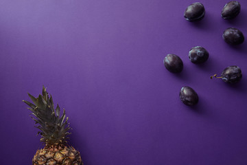 top view of pineapple and plums on violet surface