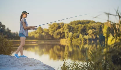 Fototapeten Cute woman is fishing with rod on lake © Dmytro Titov