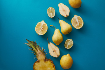 elevated view of pineapple, pears and lemons on blue surface