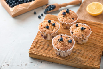Wooden board with tasty blueberry muffins on table