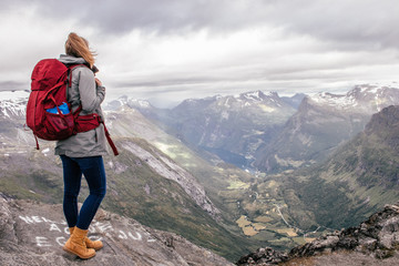 Fototapeta premium girl wandering on a mountain with a red backpack in Geiranger, Norway