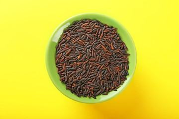 Bowl with raw wild rice on color background