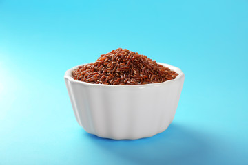 Bowl with raw red rice on color background