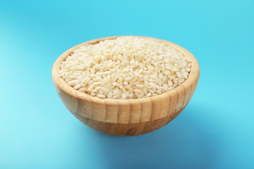 Wooden bowl with raw rice on color background